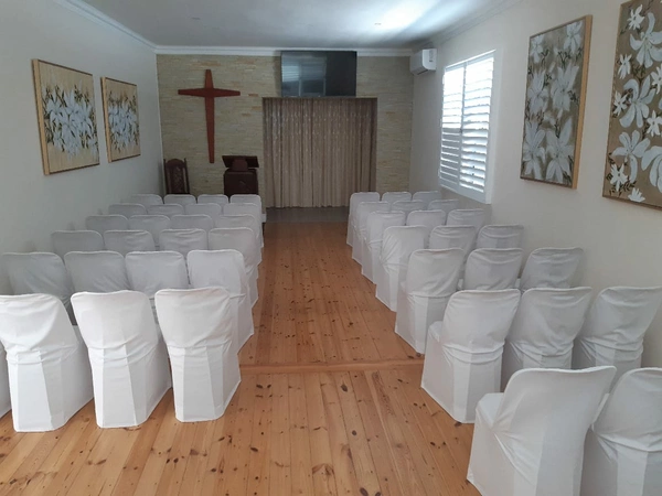 A Chapel featuring white chairs arranged neatly, with a prominent cross displayed on the wall. A Chapel featuring white chairs arranged neatly, with a prominent cross displayed on the wall.