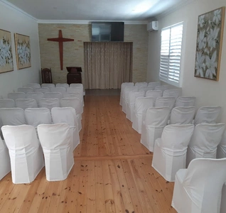 Interior view of the Chapel with white chairs arranged neatly and a cross hanging on the wall